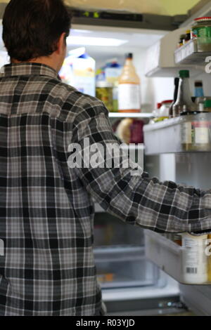 Rear View Of A Confused Young Man Looking At Food In Refrigerator. Stock Photo