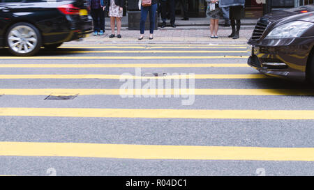 People waiting to cross street, pedestrian crossing on busy road, detail of the legs of a crowd, city daily traffic. Stock Photo