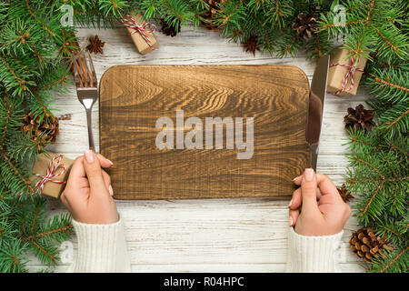 top view girl holds fork and knife in hand and is ready to eat. Empty wood rectangular plate on wooden christmas background. holiday dinner dish conce Stock Photo