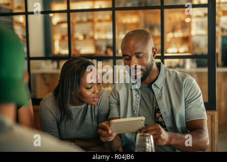 Two friends sitting in a bar looking at cellphone photos Stock Photo