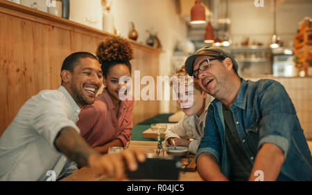 Smiling young friends sitting in a bistro taking selfies together Stock Photo