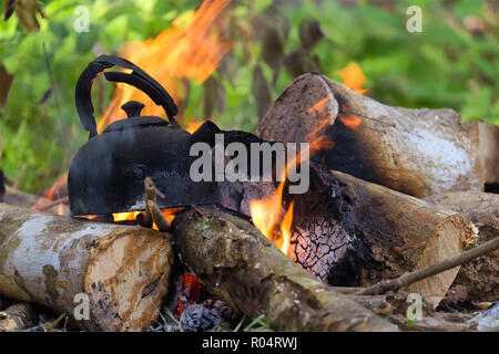 Boiling water in burnt kettle on wild campfire Stock Photo