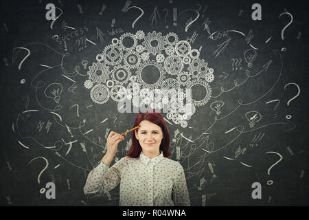 Puzzled businesswoman having questions in front of a blackboard. Big chalk drawn gear brain above head, positive thinking mess as thoughts. Concept fo Stock Photo