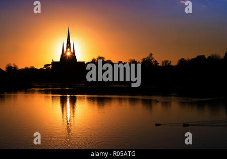02/11/18  Ahead of a cold night the setting sun shines through the central spire of Lichfield Cathedral, and is reflected in Stowe Pool.  The Staffordshire medieval cathedral  is the only English cathedral with three spires. The three spires are often referred to as 'the Ladies of the Vale'. Stock Photo