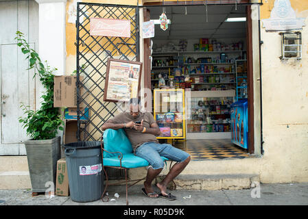 Unidentified Colombian man sits outside his shop in Getsemani, checking his mobile phone. Cartagena de Indias, Colombia. Oct 2018 Stock Photo
