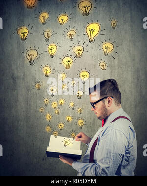 Young business man in glasses holding reading an opened book with glowing light bulbs flying out Stock Photo