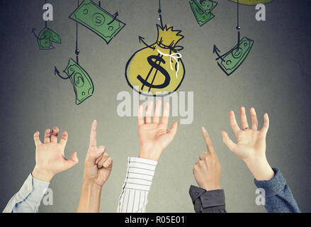 Many hands in the air trying to reach money bag hanging on the hooks. Financial concept Stock Photo