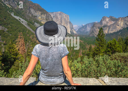 Traveler lifestyle woman with big hat contemplating Tunnel View overlook in Yosemite National Park. Relaxing at the popular El Capitan and Half Dome overlook. Travel holidays in California, Usa. Stock Photo