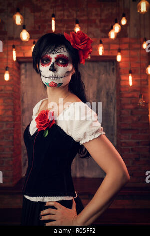 Portrait of woman halloween with white make-up on her face, sewn on mouth, black eyes on gloomy background of brick wall with burning lights Stock Photo