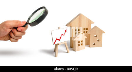 Magnifying glass is looking at the Wooden houses stand with red arrow up. Growing demand for housing and real estate. The growth of the city and its p Stock Photo