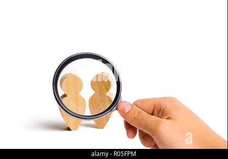Magnifying glass is looking at the Two people stand together and talk. Three wooden figures of people conduct a conversation on a blue background. Pla Stock Photo