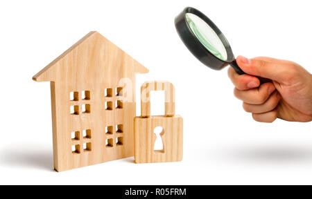 Magnifying glass is looking at the Wooden house padlock. The concept of protection of property and real estate, property rights. Installation of alarm Stock Photo