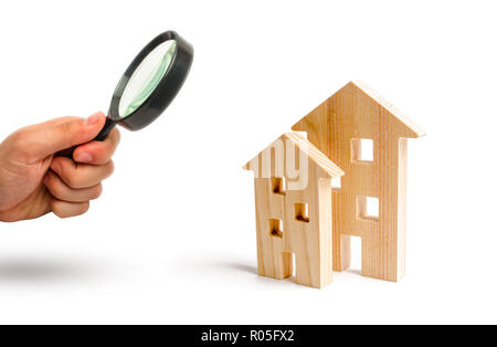 Magnifying glass is looking at the Wooden houses on a white background. Growing demand for housing and real estate. The growth of the city and its pop Stock Photo