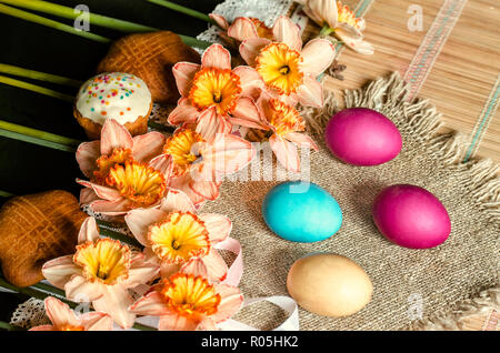Large pink daffodils with yellow fringe in the middle and biscuits on burlap with painted Easter eggs lie on straw carpet Stock Photo