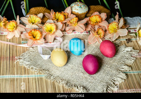 Pink daffodils with yellow fringe in the middle and biscuits on burlap with painted Easter eggs lie on straw carpet Stock Photo