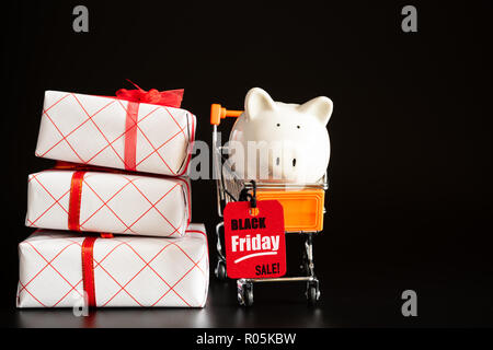 Shopping sale concept with red ticket Black Friday Sale tag hanging with piggy bank on shopping cart with stack of gift boxes. Stock Photo