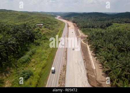 Rural road under construction across palm oil plantation . The road is under upgrading to dual carriage lane called Pan Borneo Highway connecting majo Stock Photo