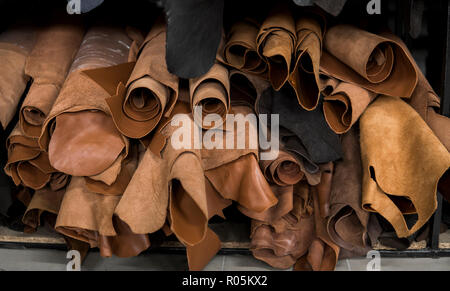 Different pieces of leather in a rolls. The pieces of the colored leathers. Rolls of natural brown red leather. Raw materials for manufacture of bags, shoes, clothing and accessories. Stock Photo