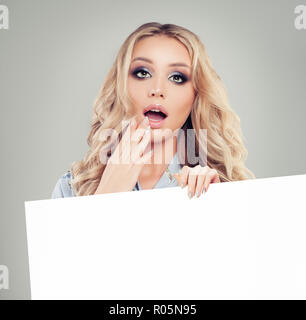 Surprised woman showing white empty paper board banner with copy space background for advertising marketing, seo or product placement Stock Photo
