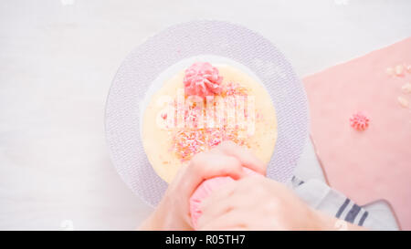 Step by step. Flat lay. Piping pink italian buttercream icing on top of a tall birthday cake. Stock Photo
