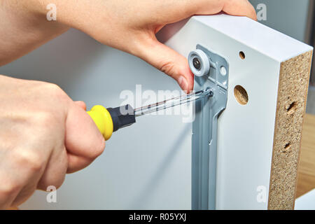 The furniture assembler is tightening the screw in the drawer slide brackets with a screwdriver, flat pack furniture assembly. Stock Photo