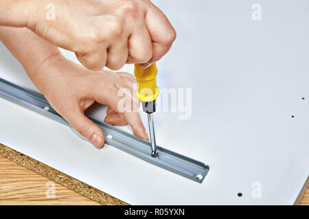 The furniture assembler tightens the drawer slides to the table, with one hand he holds the drawer slides, with his other hand he tightens the screw w Stock Photo