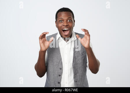 Portrait of an african excited casual man standing with raised hands and looking at camera Stock Photo