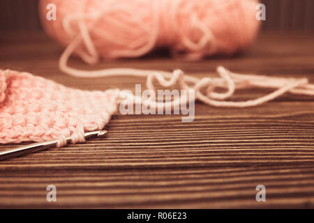selective focus of pink knitted wool yarn and crocheted on wood background. Stock Photo