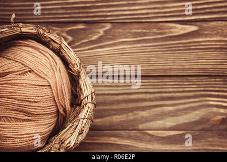 top view of brown woolen tangles of threads in wicker basket on wooden knitting background. Stock Photo