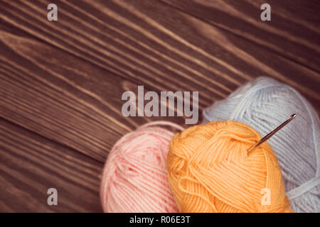 top view of blue and pink yellow wool balls of thread and crochet hook on wooden knitting background. Stock Photo
