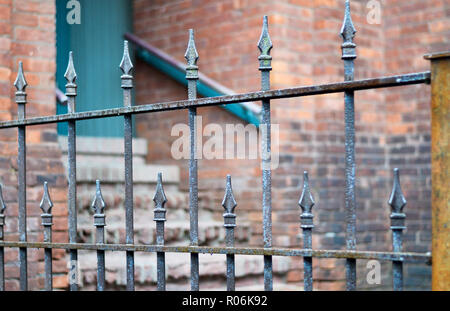 Antique Wrought Iron Fence with Selective Focus. Brick Wall with Doorway and Staircase in  the Background. Stock Photo