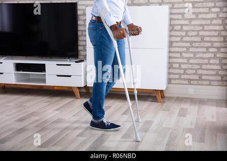 Low Section View Of A Disabled Man Walking With Crutches At Home Stock Photo