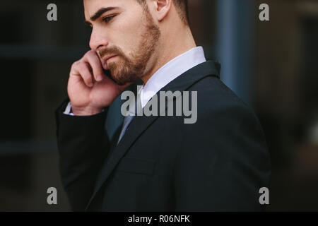 businessman talking over mobile phone. Young business professional looking busy talking on mobile phone outdoors. Stock Photo