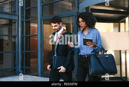 Two business colleagues walking out of office building. Corporate business professionals walking together and talking. Stock Photo