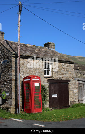 Iconic red telephone box in front of traditional stone building in Thwaite, a small village in Swaledale, Yorkshire Dales, North Yorkshire, England UK Stock Photo