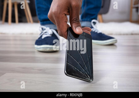 Man's Hand Picking Up Mobile Phone With Broken Screen Stock Photo