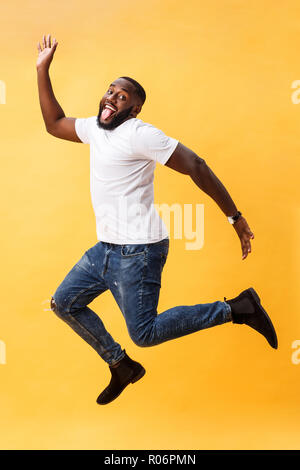 Full length of handsome young black man jumping against yellow background. Stock Photo