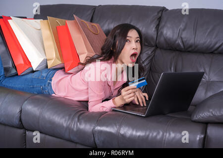 shocked woman using laptop computer for online shopping with credit card in the living room Stock Photo