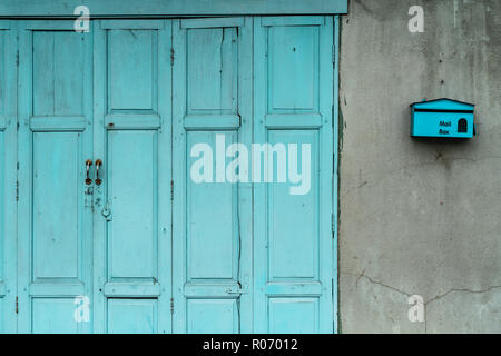 Closed green or blue wooden door and empty mail box on cracked concrete wall of house. Old home with cracked cement wall. Vintage front door abstract  Stock Photo