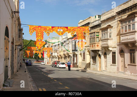 Marsa, Malta - May 2018: Festively decorated street with policemen and old traditional balconies. Banners for annual festa religious holiday in sunny  Stock Photo