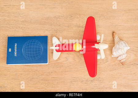 Passport, toy plane and shell lying on a wooden table as a concept of relaxing by the sea Stock Photo