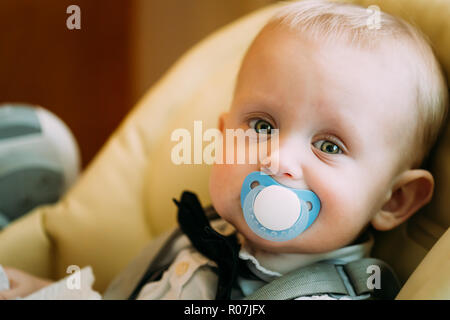 Pretty Baby Boy With Big Green Eyes Sitting In Yellow Seat With Soother Stock Photo