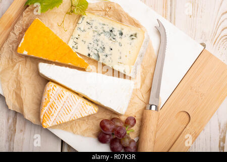 Tasting plate with four France cheeses, cream brie, marcaire, saint paulin and blue auvergne cheese, served with fresh ripe grapes close up Stock Photo