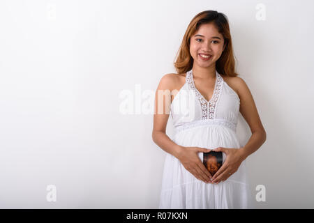 Studio shot of young happy Asian pregnant woman smiling while ho Stock Photo