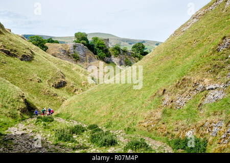 Walkers descending the stony path of Limestone Way in Cave Dale, with Peveril Castle in the distance, Derbyshire, Peak District, England, UK Stock Photo