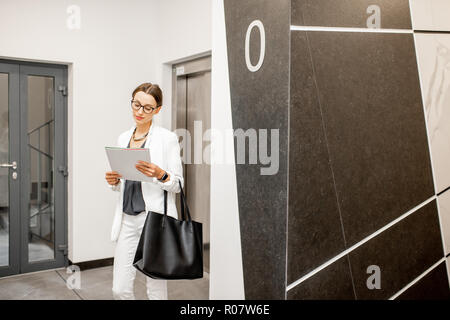 Young business woman in white suit standing in the walkhall near the elevator at the modern residential building Stock Photo