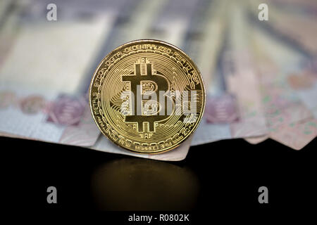 Bitcoin token on black with reflection, on top of Dubai, dirham banknotes money. Cryptocurrency versus paper currency concept Stock Photo