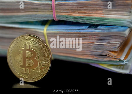 Bitcoin token on black with reflection, with a big pile of euro banknote money in the background Stock Photo