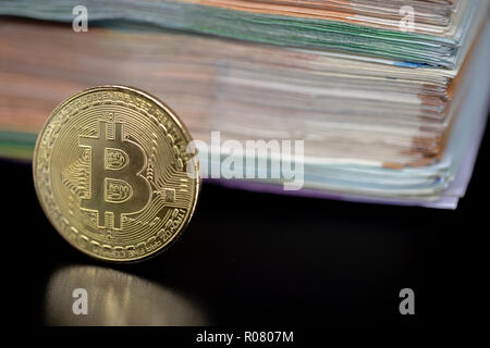 Bitcoin token on black with reflection, with a big pile of euro banknote money in the background Stock Photo
