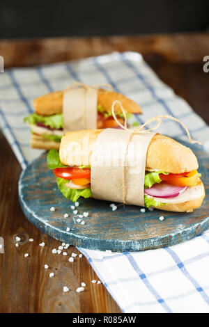 Appetizing sandwich from crispy bread with chicken, tomatoes, lettuce, cheese and spices on a dark wooden background. Restaurant and menu concept. Stock Photo